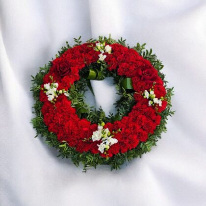 Coroană funerară rotundă cu garoafe roșii, trandafiri și frezii